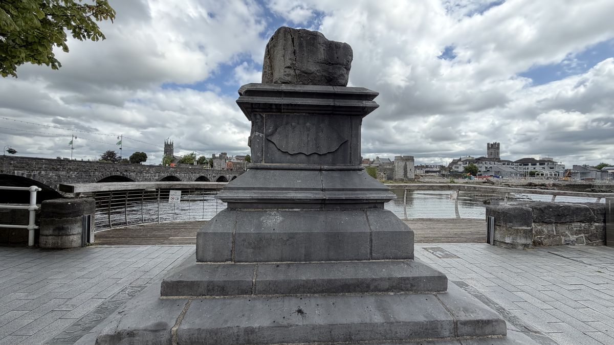 Primer plano de la Piedra del Tratado sobre su pedestal de 1865, con el puente de Thomond al fondo