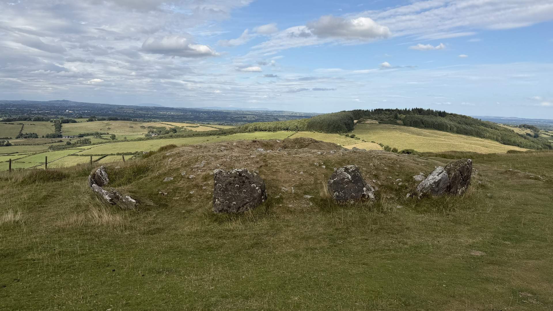 Vista panorámica desde Loughcrew con un pequeño cairn satélite en primer plano y el paisaje de Meath extendiéndose hacia el horizonte