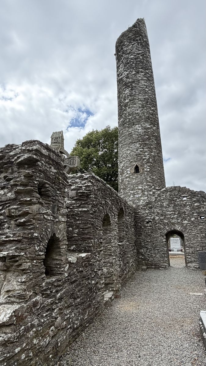 La torre redonda de Monasterboice asomando tras un muro en ruinas del monasterio