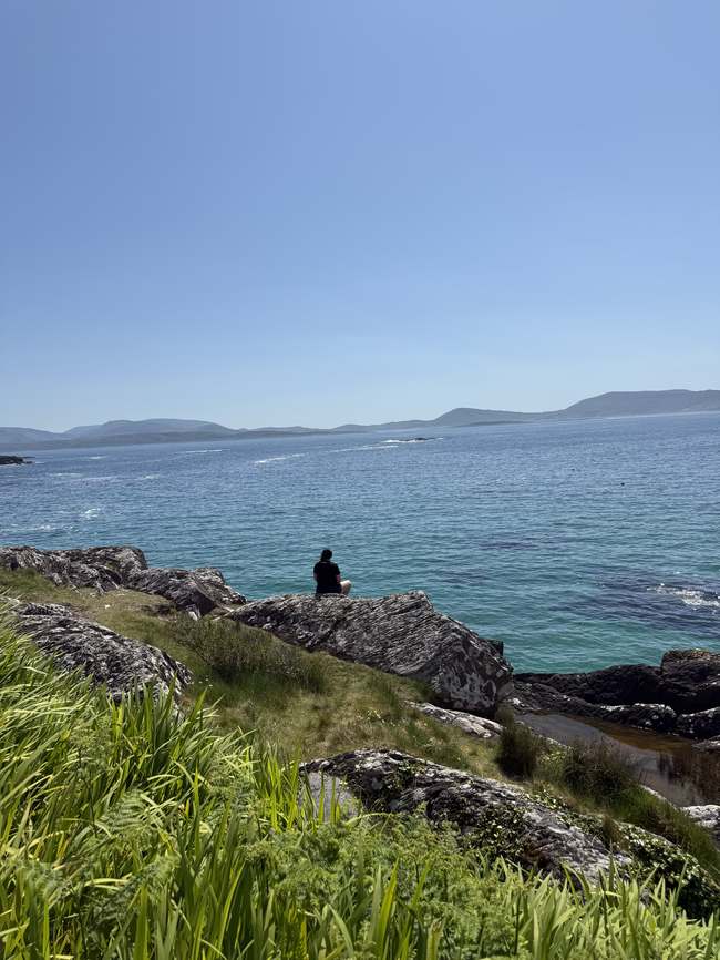 Una persona contemplando el mar turquesa desde las rocas de Carrol's Cove, cerca de Derrynane