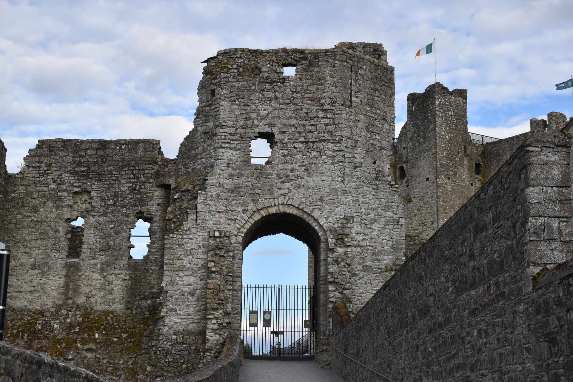 Arco de una de las puertas en ruinas del Castillo de Trim, con la bandera irlandesa ondeando sobre la torre al fondo